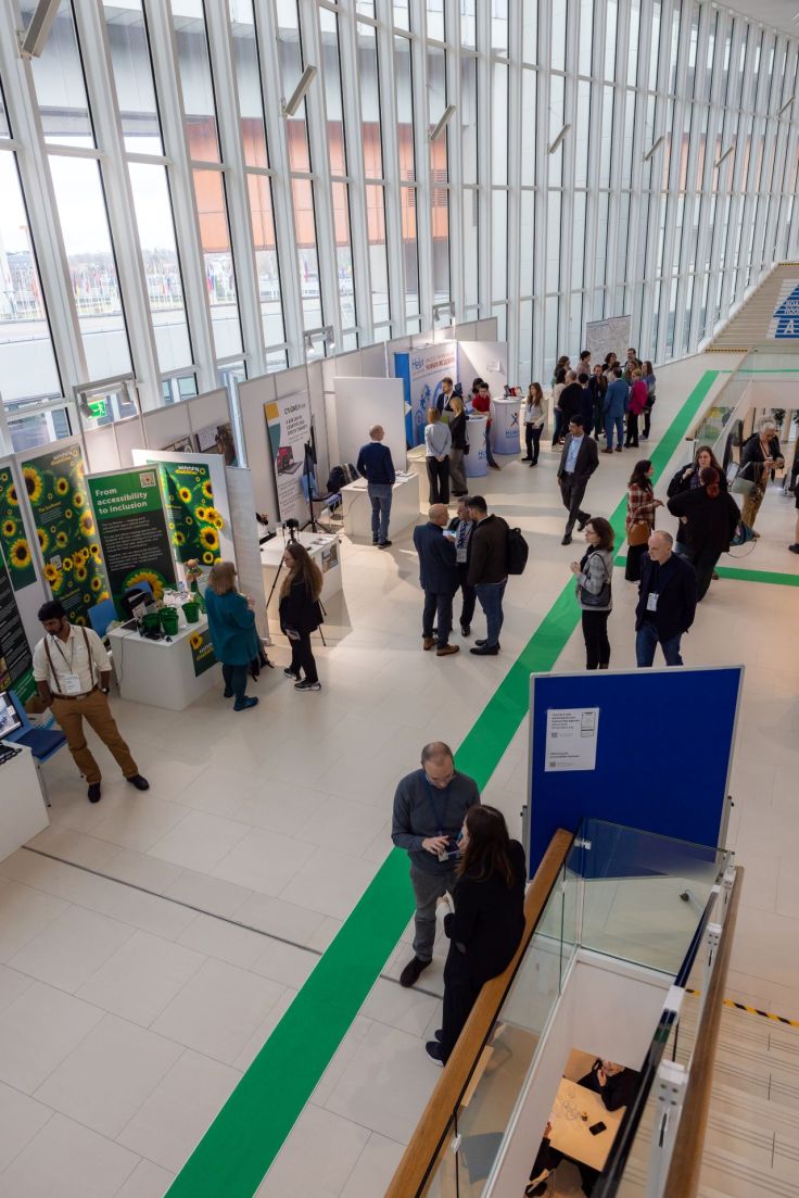 the 1st floor of the M-building of the VIC, picture taken from above, with a view of the booths. The DIN booth is the last one with a lot of DIN members standing in front of it.