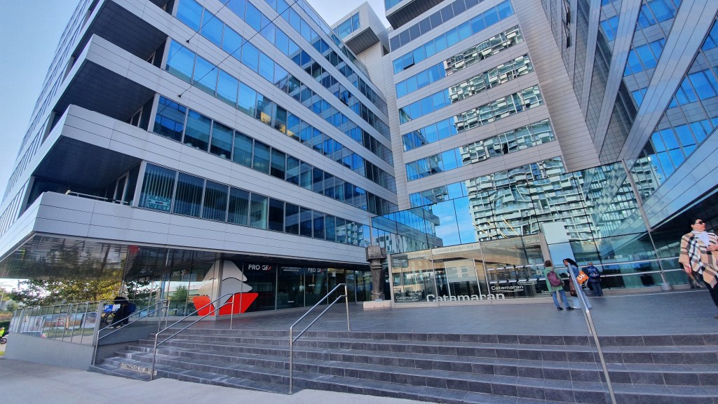 Modern glass-and-steel office building with a wide stone staircase leading to the entrance marked “Catamaran”.