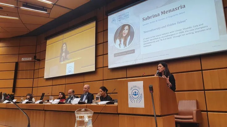 Sabrina Menasria speaking on the podium of CR1, with the other speakers sitting at the podium